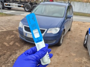 narkotest w dłoni, na którą jest założona gumowa rękawiczka. W tle granatowy vw touran