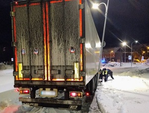 na dworze ciemno. Na zaśnieżonej jezdni stoi ciężarówka z naczepą. Dotyka przechylonej lampy. Policjant łopatą odgarnia śnieg spod kół ciężarówki
