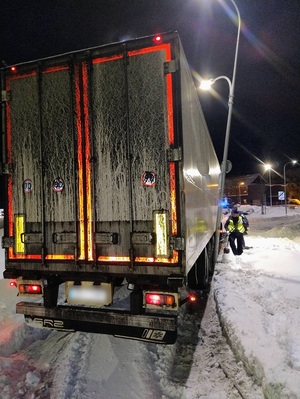 na dworze ciemno. Na zaśnieżonej jezdni stoi ciężarówka z naczepą. Dotyka przechylonej lampy. Obok stoi policjant trzymający łopatę