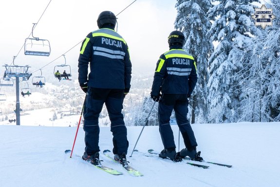 dwaj policjanci na nartach na stoku. Nad nimi wyciąg narciarski