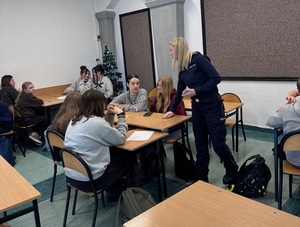 w klasie szkolnej policjantka rozdaje ulotki siedzącym w ławkach uczniom