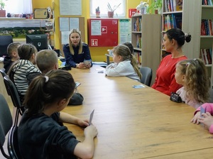 w bibliotece przy stole siedzą dzieci, opiekunka i policjantka