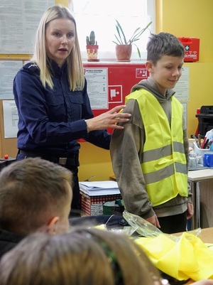 w bibliotece policjantka prezentuje dzieciom prawidłowy sposób noszenia kamizelki odblaskowej, którą ma na sobie chłopiec