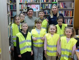 biblioteka. Zdjęcie grupowe dzieci ubranych w kamizelki odblaskowe, opiekunki i policjantki