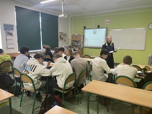 klasa szkolna. Przed siedzącymi w ławkach uczniami stoi policjantka