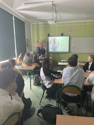 klasa szkolna. Przed siedzącymi w ławkach uczniami stoi policjantka