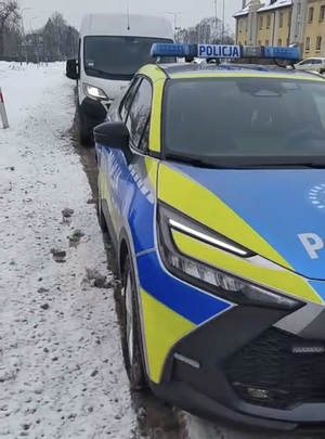 na poboczu stoi oznakowany policyjny radiowóz. Za nim stoi bus