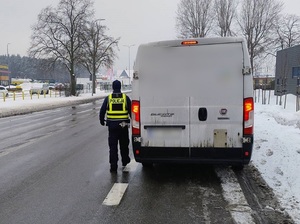na poboczu stoi biały bus. Obok stoi policjant ruchu drogowego