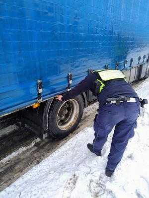 policjant ruchu drogowego sprawdza stan opony w samochodzie ciężarowym