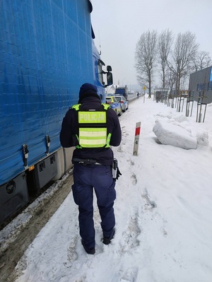 na poboczu stoi pojazd ciężarowy. Obok idzie policjant ruchu drogowego