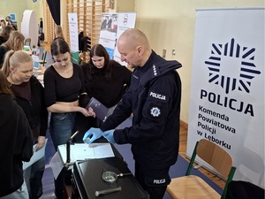 w sali sportowej przy policyjnym stoisku technik kryminalistyki prezentuje zgromadzonej młodzieży sposób zabezpieczania linii papilarnych