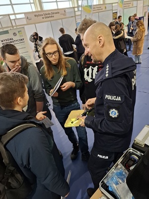 w sali sportowej przy policyjnym stoisku technik kryminalistyki prezentuje zgromadzonej młodzieży sposób ujawniania śladów traseologicznych