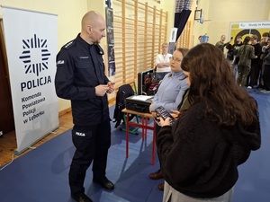 w sali sportowej przy policyjnym stoisku technik kryminalistyki rozmawia z dwiema uczennicami