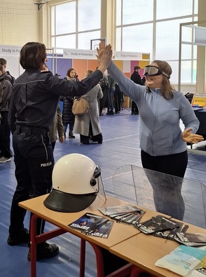 w sali sportowej przy policyjnym stoisku policjantka przybija piątkę z uczennicą, która ma założone narkogogle