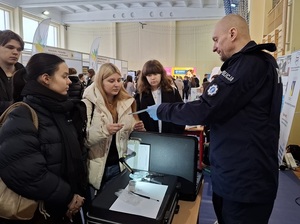 w sali sportowej przy policyjnym stoisku technik kryminalistyki prezentuje zgromadzonej młodzieży sposób zabezpieczania śladów