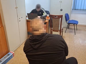 w pokoju przesłuchań na krześle siedzi mężczyzna. Przed nim przy biurku siedzi nieumundurowany policjant służby kryminalnej
