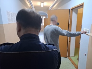 do celi wchodzi zatrzymany mężczyzna. Za nim stoi policjant służby dyżurnej