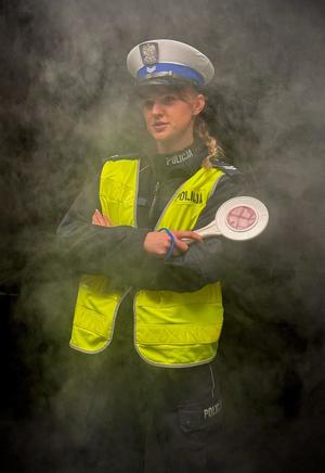 na czarnym zadymionym tle stoi policjantka ruchu drogowego, trzymająca tarczę do zatrzymywania pojazdów