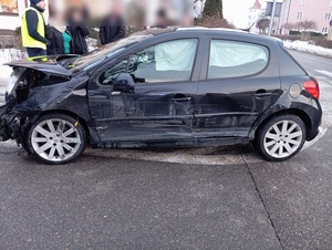 na jezdni przy chodniku, na powierzchni wyłączonej z ruchu stoi uszkodzone ciemne osobowe auto z wgniecioną maską i przerysowanym bokiem. Obok stoi policjant ruchu drogowego w towarzystwie kilku osób