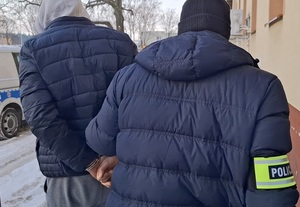 policjant kryminalny wyprowadza z budynku komendy mężczyznę, który ma ręce skute za plecami kajdankami