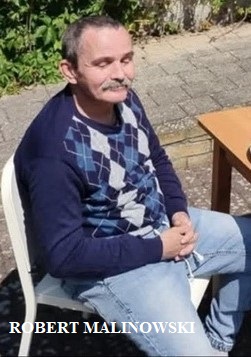 kolorowe zdjęcie przedstawiające siedzącego na dworze na krześle mężczyznę w średnim wieku z ciemnymi włosami i wąsami