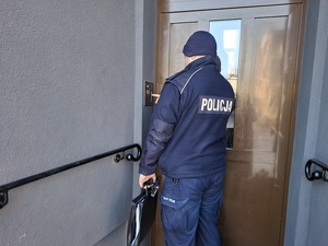 dzielnicowy przed drzwiami wejściowymi do budynku, dzwoni domofonem