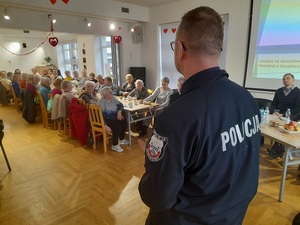 dzielnicowy przed grupą seniorów siedzących na krzesłach na sali w klubie seniora