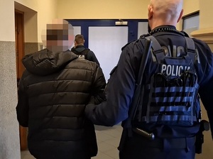 policjant prowadzi korytarzem zatrzymanego mężczyznę