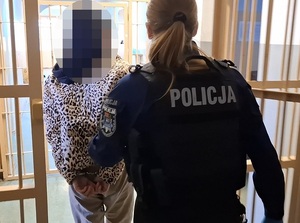 policjantka prowadzi korytarzem pomieszczenia dla osób zatrzymanych kobietę, która ma ręce skute kajdankami