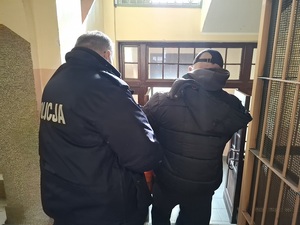 policjant prowadzi mężczyznę schodami w dół w kierunku wyjścia z budynku komendy