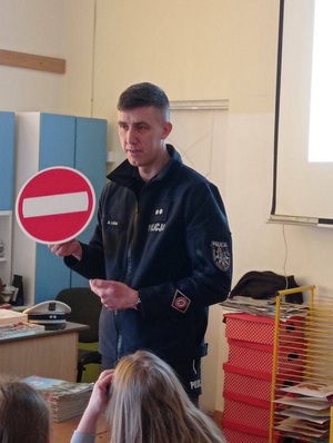 policjant ruchu drogowego w szkolnej klasie, trzymający znak drogowy "zakaz wjazdu"