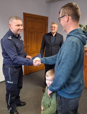 w gabinecie Komendanta Powiatowego Policji w Lęborku komendant ściska dłoń mężczyzny, przy którym stoi kilkuletni chłopiec. Obok stoi uśmiechnięty zastępca komendanta
