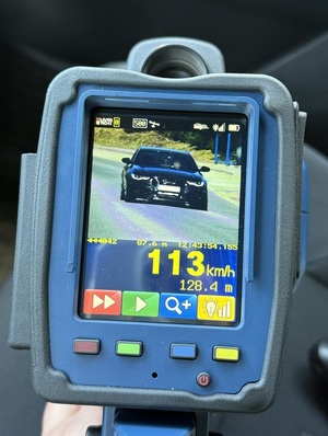 ekran ręcznego miernika prędkości, na którym widać czarne osobowe Audi i wyświetloną prędkość tego auta: 113 km/h
