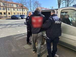 dwaj policjanci wprowadzają do nieoznakowanego radiowozu zatrzymanego mężczyznę