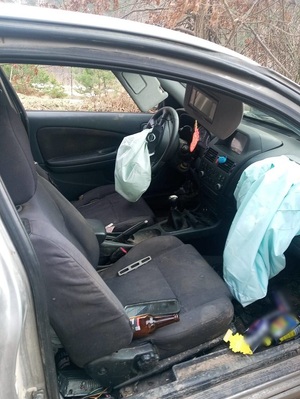 wnętrze samochodu. Wystrzelone przednie poduszki powietrzne. W środku nieład. Na podłodze leżą puszki, na przednim siedzeniu pusta butelka po piwie i telefon komórkowy