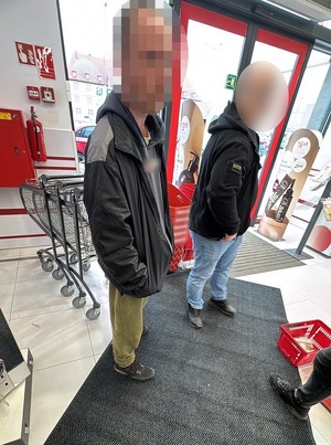 w drogerii przy drzwiach wyjściowych stoi mężczyzna. Obok niego stoi nieumundurowany policjant. Na podłodze znajduje się koszyk sklepowy wypełniony opakowaniami kleju do protez zębowych