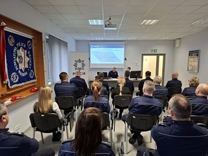 w auli przy stole siedzą Komendant Powiatowy Policji w Lęborku i Zastępczyni Komendanta Wojewódzkiego Policji w Gdańsku. Komendant omawia wyniki osiągnięte w ubiegłym roku. Naprzeciw siedzą policjanci