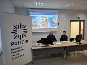 w auli przy stole siedzą Komendant Powiatowy Policji w Lęborku i Zastępczyni Komendanta Wojewódzkiego Policji w Gdańsku. Komendant omawia wyniki osiągnięte w ubiegłym roku.