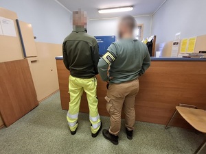 w pomieszczeniu depozytowym przy blacie stoi zatrzymany mężczyzna. Obok niego stoi policjant służby kryminalnej