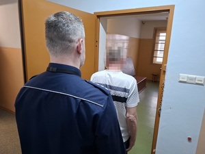 w otwartych drzwiach celi stoi zatrzymany mężczyzna. Za nim stoi policjant służby dyżurnej