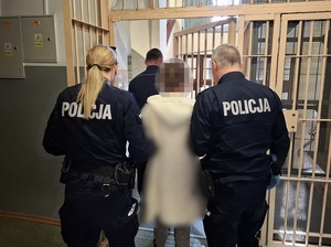 dwoje policjantów wyprowadza kobietę z pomieszczenia dla osób zatrzymanych