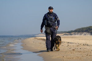 policjant z psem służbowym na smyczy idzie brzegiem morza