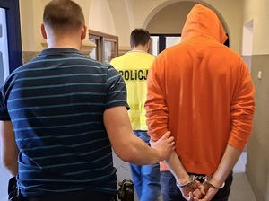 nieumundurowany policjant prowadzi korytarzem w komendzie mężczyznę, który ma ręce skute za plecami kajdankami