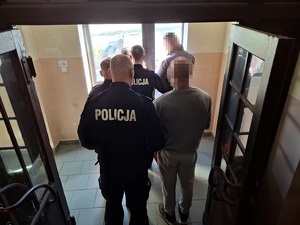 trzech policjantów sprowadza schodami w dół w kierunku wyjścia z komendy dwóch zatrzymanych mężczyzn