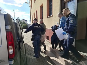 dwaj policjanci wychodzą z dwoma zatrzymanymi mężczyznami z budynku komendy. Kierują się w stronę nieoznakowanego radiowozu