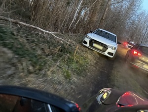 w zagajniku na drodze gruntowej na trawie jest zaparkowany biały osobowy samochód. Obok stoją dwa policyjne radiowozy