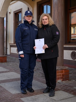 przed budynkiem poczty w Łebie stoją obok siebie: policjantka dzielnicowa i listonoszka w cywilnym ubraniu, trzymająca w dłoni dyplom