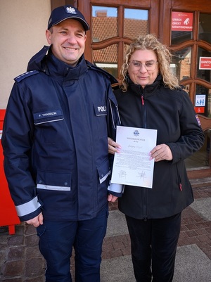 w Łebie przed budynkiem poczty stoją obok siebie komendant komisariatu policji i listonoszka w cywilnym ubraniu, trzymająca dyplom