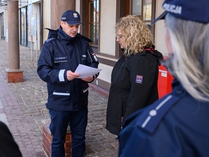 w Łebie przed budynkiem poczty komendant komisariatu policji odczytuje podziękowania dla stojącej przed nim listonoszki