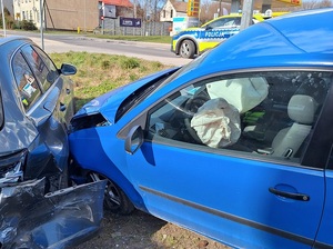 miejsce zdarzenia drogowego. Poza jezdnią na pasie zieleni niebieski Vw Polo wjechał w bok szarego osobowego samochodu. Oba pojazdy mają wgniecioną karoserię. W Vw wystrzeliły poduszki powietrzne. Na jezdni stoi oznakowany policyjny radiowóz